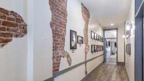 A hallway with exposed brick walls, framed pictures, and a wooden floor.