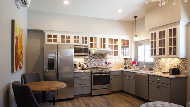 A modern kitchen with stainless steel appliances, a wooden dining table, and a tufted ottoman.