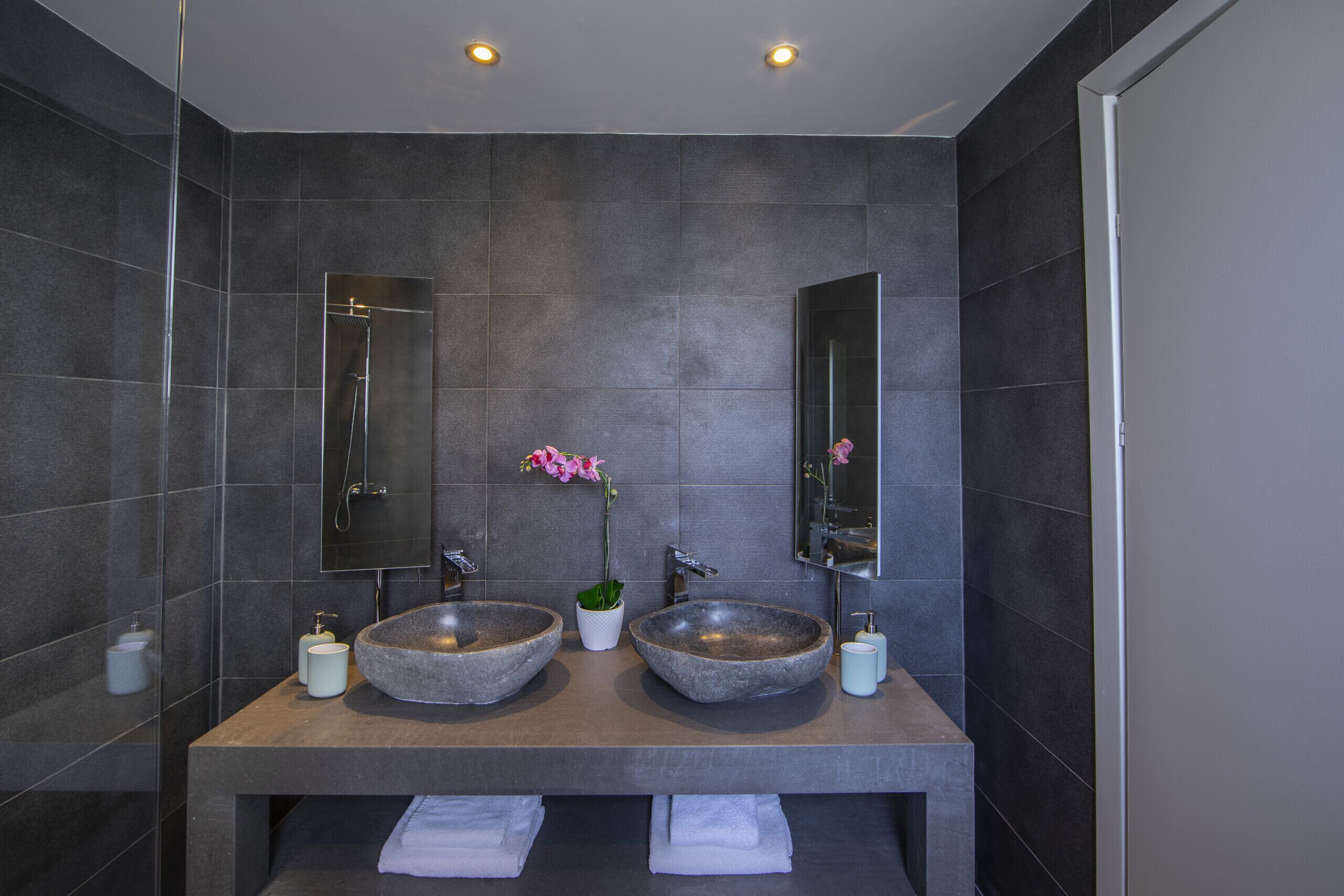 Een moderne badkamer met twee stenen wasbakken, een spiegel en een potorkidee.