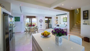 A modern kitchen with a central island, a dining area with a table and chairs, and a living space with a sofa and a staircase. - Protaras Seafront Villa El Greco (Protaras)