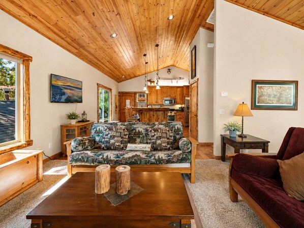 Una sala de estar acogedora con techo de madera, un sofá con un estampado de bosque, una mesita de centro y un sofá rojo.