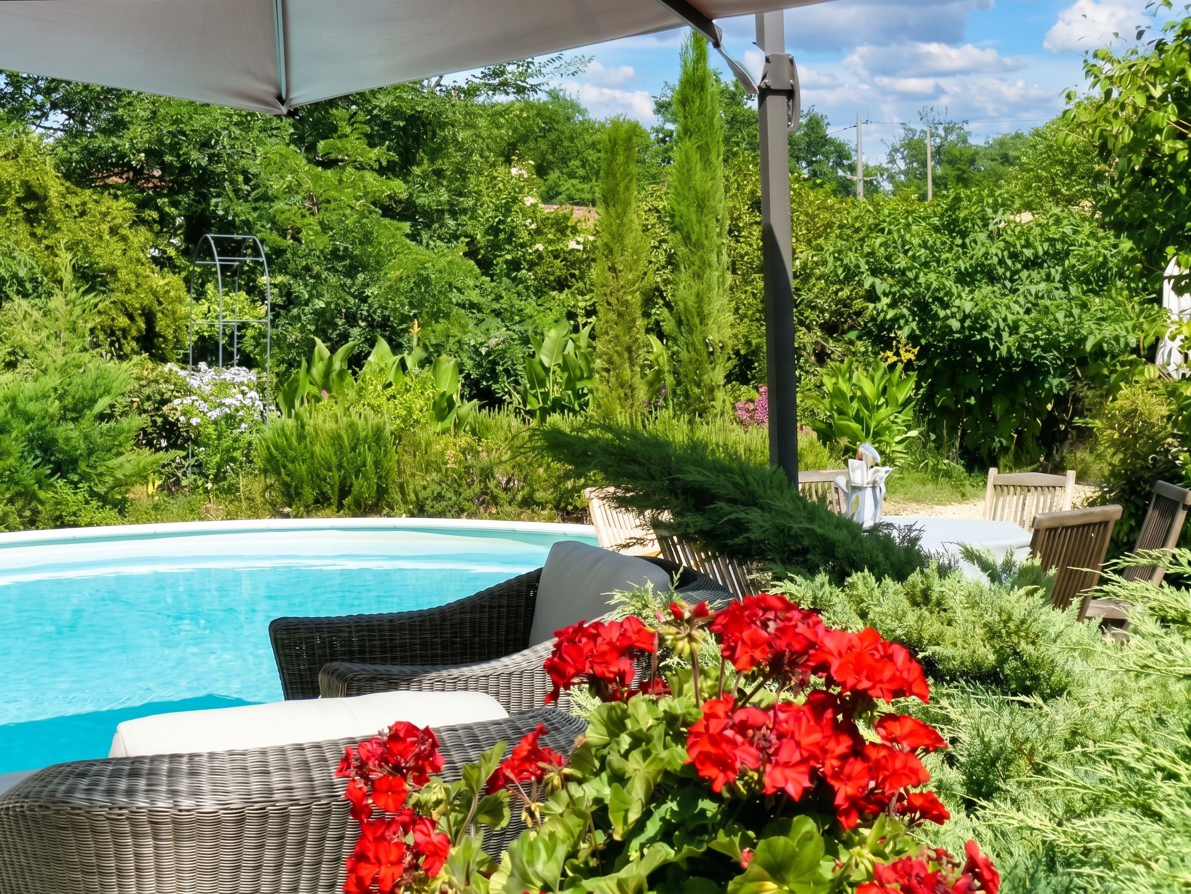 A poolside area with a wicker lounge chair, red flowers, and lush greenery.