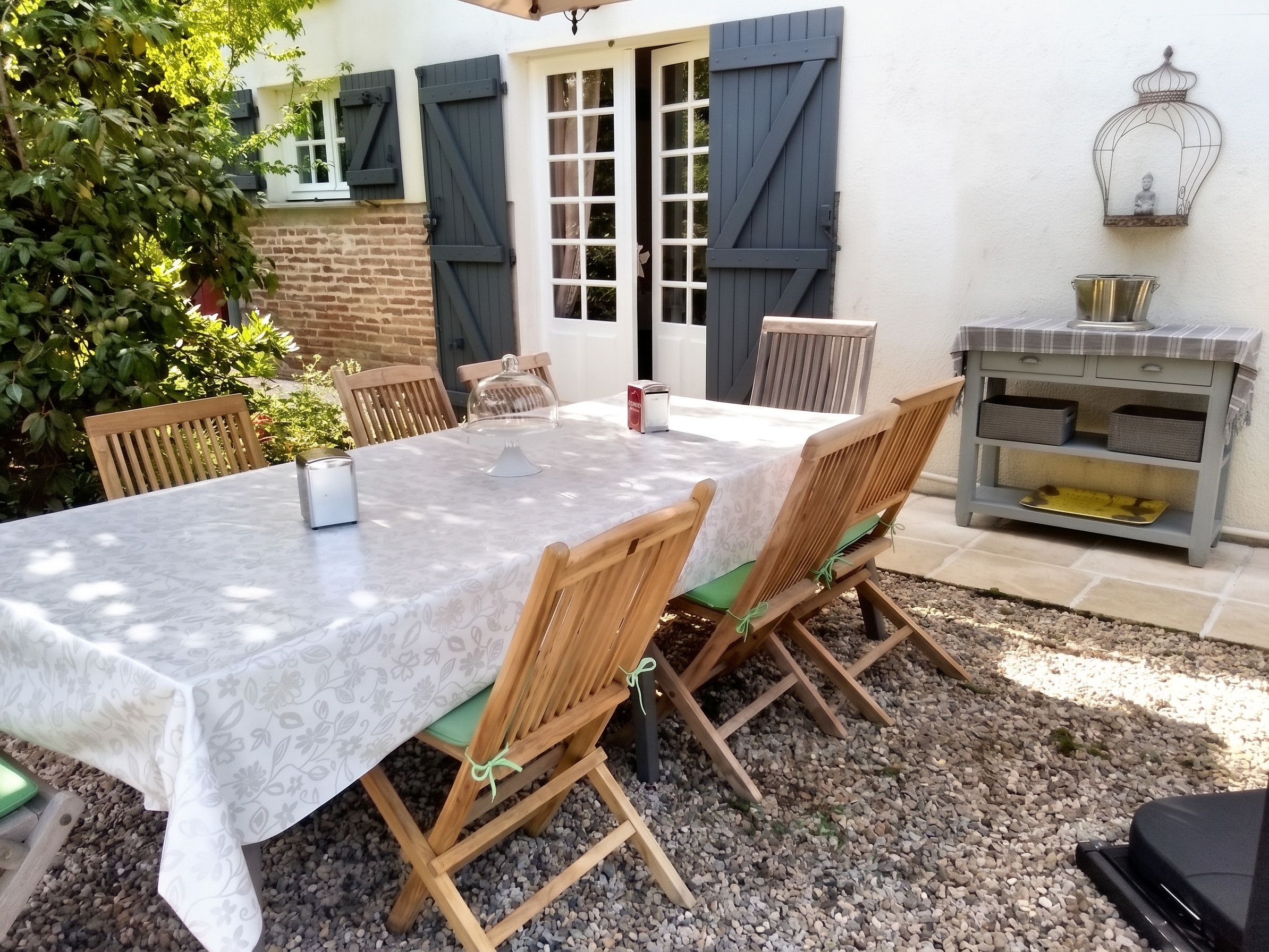 Een terras buiten met een tafel, stoelen, een barbecue en een bakstenen muur.