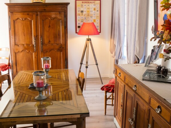 A dining area with a wooden table, chairs, a cabinet, a lamp, and a poster on the wall. - Homerez - Villa in Arsac with pool (Arsac)