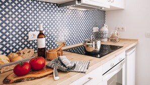 A kitchen with a patterned backsplash, a wooden countertop, a cutting board with tomatoes and bread, a knife, a bottle of olive oil, a pot, and a coffee maker.