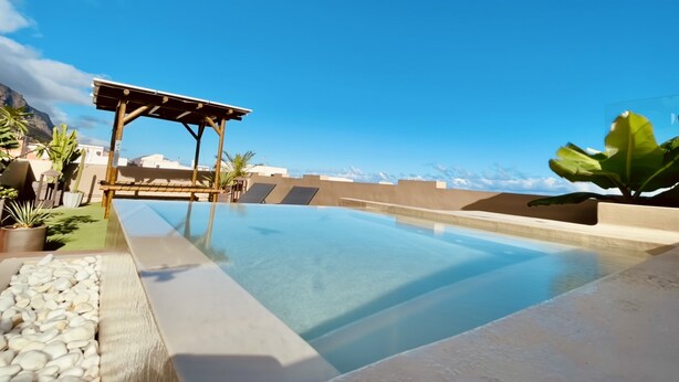 A rooftop infinity pool with a pergola, potted plants, and a view of the mountains.