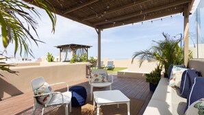 An outdoor patio with white furniture, a thatched roof, and a view of the sea.