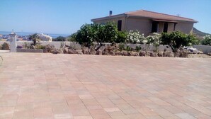Un ampio patio con pavimento piastrellato, un muro in pietra e un edificio con tetto rosso sullo sfondo.