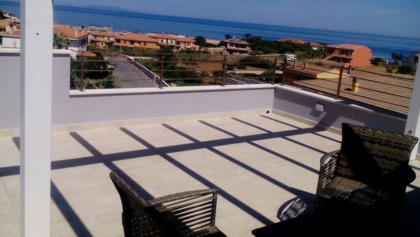 Un balcone con due sedie in vimini, vista sul mare e edifici sullo sfondo.