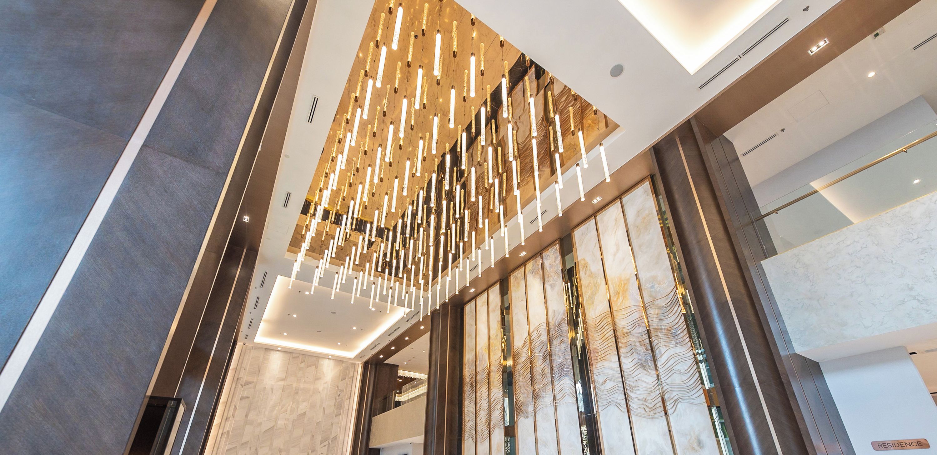 Un hall d’hôtel moderne avec un plafond haut, un comptoir d’accueil et une grande cloison en verre.