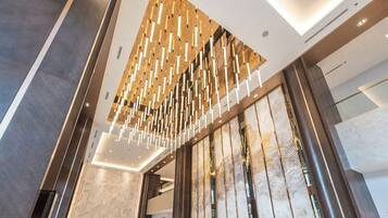 Un hall d’hôtel moderne avec un plafond haut, un comptoir d’accueil et une grande cloison en verre.