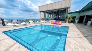Una piscina en la azotea con vistas despejadas del horizonte de la ciudad, rodeada de modernas sillas de descanso y plantas en macetas.