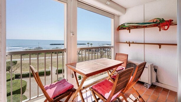 Een balkon met een tafel en stoelen, met uitzicht op een strand en de oceaan.