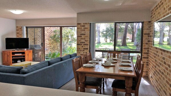 A modern living room with a dining area, large windows, and a brick wall.