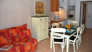 Ett kompakt bostadsutrymme med en soffa, ett matbord, stolar, ett köksutrymme med en kaffebryggare och ett skåp.