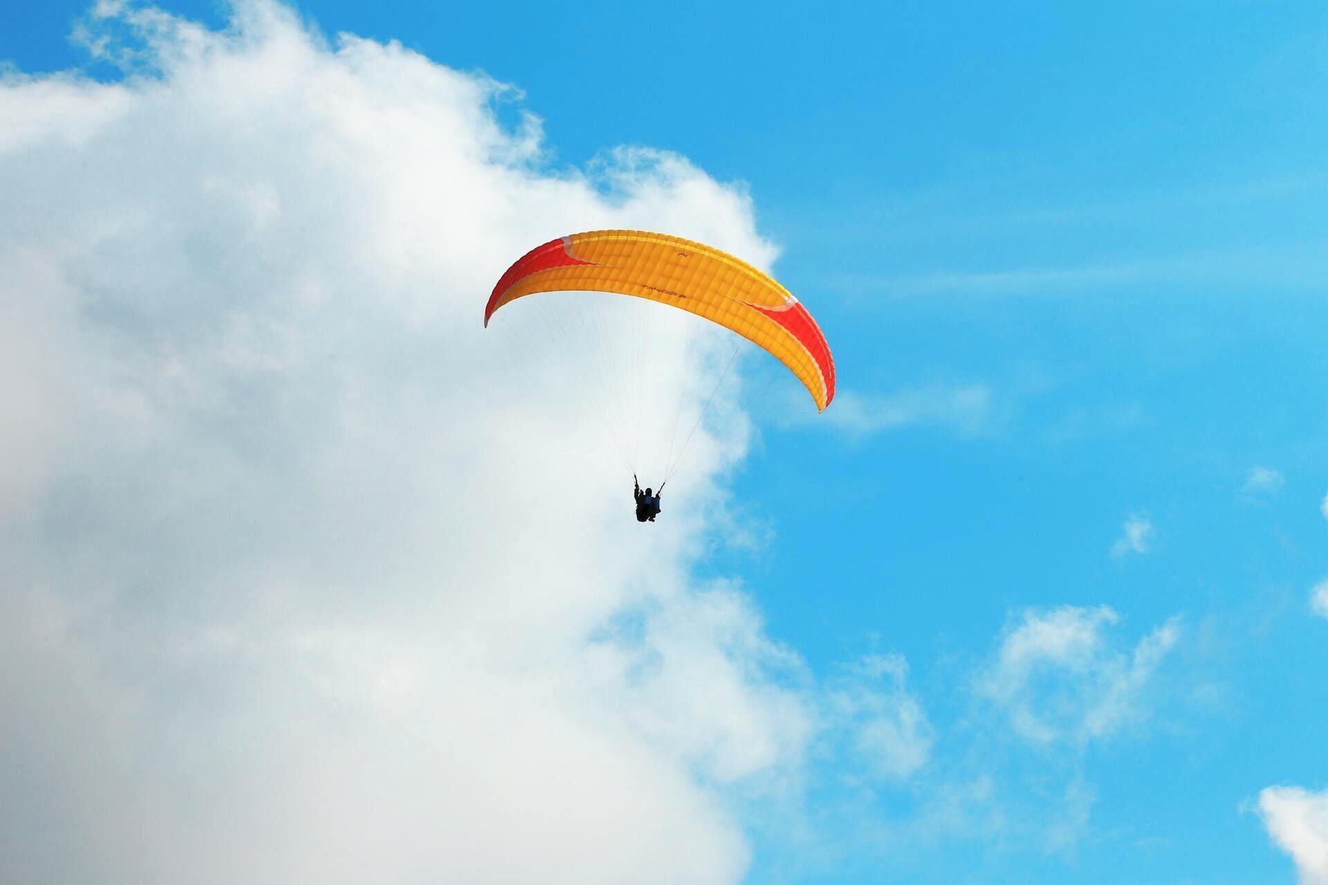 Un parapente avec un parachute jaune et rouge, sur fond de ciel bleu et de nuages.