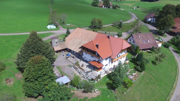 Una casa a due piani con tetto in tegole rosse, circondata da campi verdi e alberi.