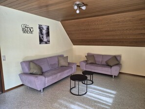A room with two purple sofas, a ceiling fan, and a framed picture on the wall.