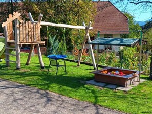 Un parc infantil amb balancins, tobogan i una cadira blava.