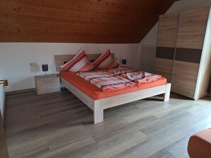 A bedroom with a wooden ceiling, a bed with striped pillows, a nightstand, and a wardrobe.