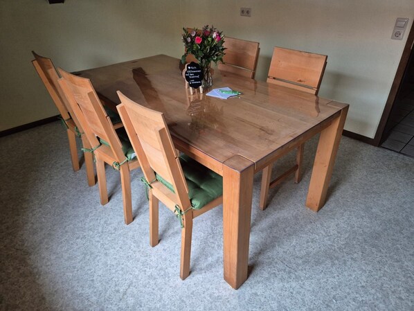 A wooden dining table with six chairs, a vase with flowers, and a sign on the table.