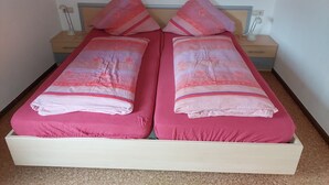 Un lit double avec une literie rose et des oreillers assortis, une tête de lit en bois, une table de chevet avec une lampe et une petite table de nuit avec une lampe.