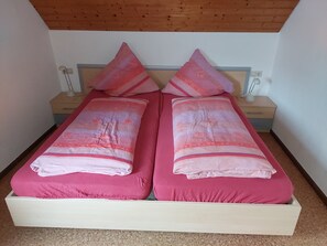 Un lit double avec une literie rose et des oreillers assortis, une tête de lit en bois, une table de chevet avec une lampe et une petite table de nuit avec une lampe.