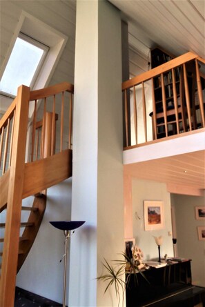 A wooden staircase leading to a lofted area with a skylight, a floor lamp, and a desk with a plant.