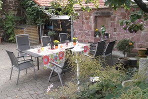 Un patio exterior con una mesa lista para comer, rodeado de sillas y macetas con plantas.