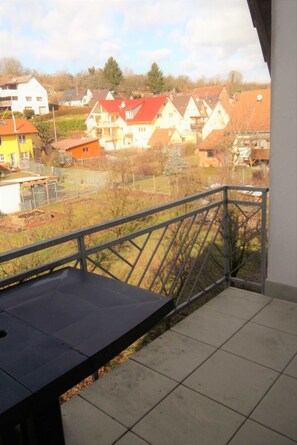 A balcony with a metal railing, a view of houses, and a clear sky.