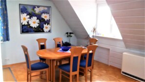 Spisestue med et rundt bord, seks stole og et blomsterbillede på væggen.