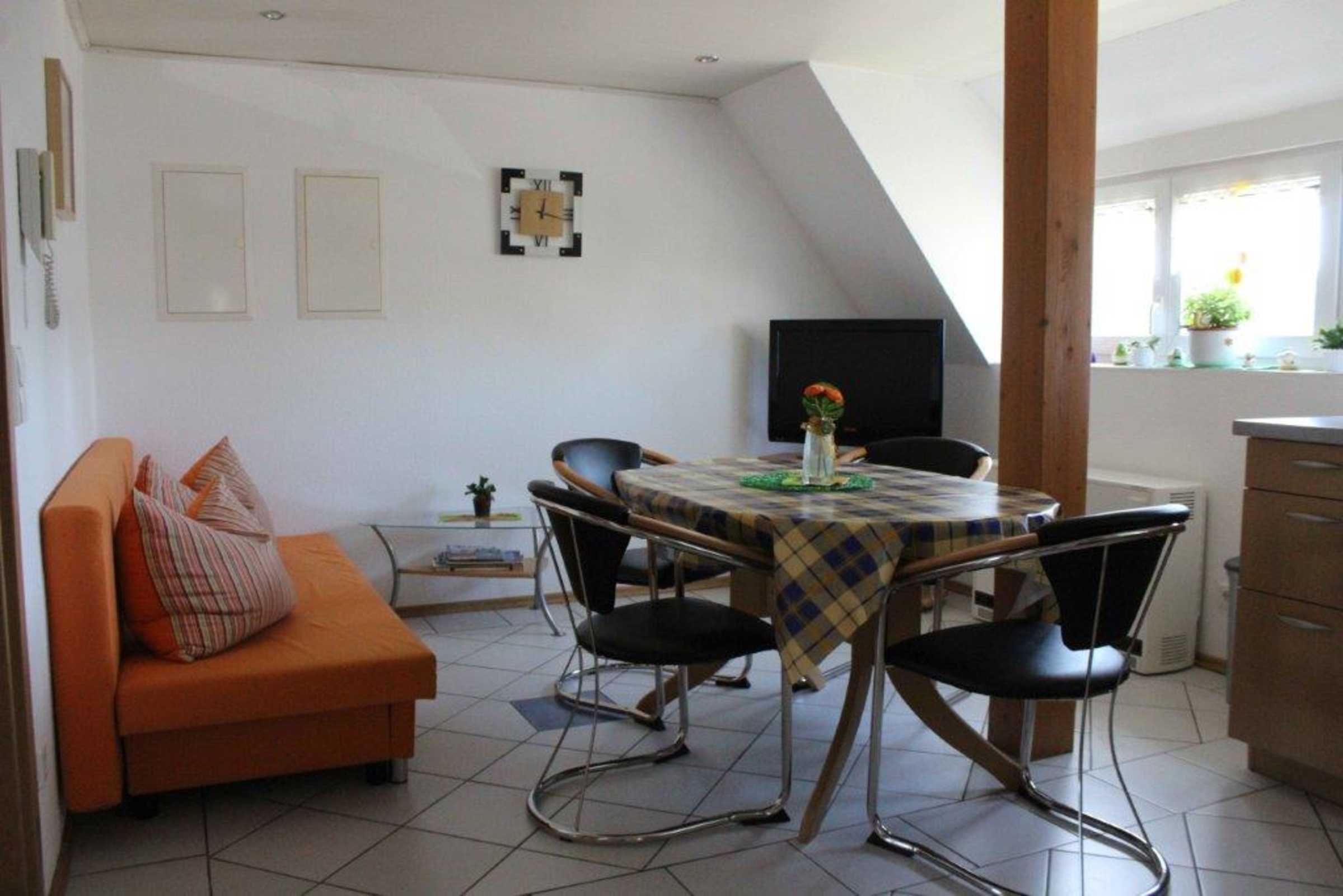A dining area with a table set for four, surrounded by chairs, in a room with a sloped ceiling and a sofa with cushions.