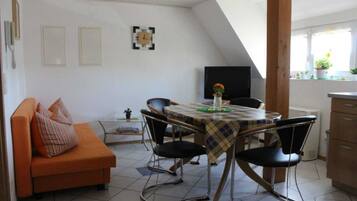 A dining area with a table set for four, surrounded by chairs, in a room with a sloped ceiling and a sofa with cushions.