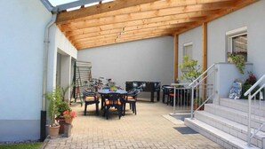 An outdoor patio area with a wooden pergola, a dining table with chairs, a grill, and potted plants. - Apartment Hug - Apartment, 4 bedrooms, from 5 persons, max. 7 people (Ringsheim)