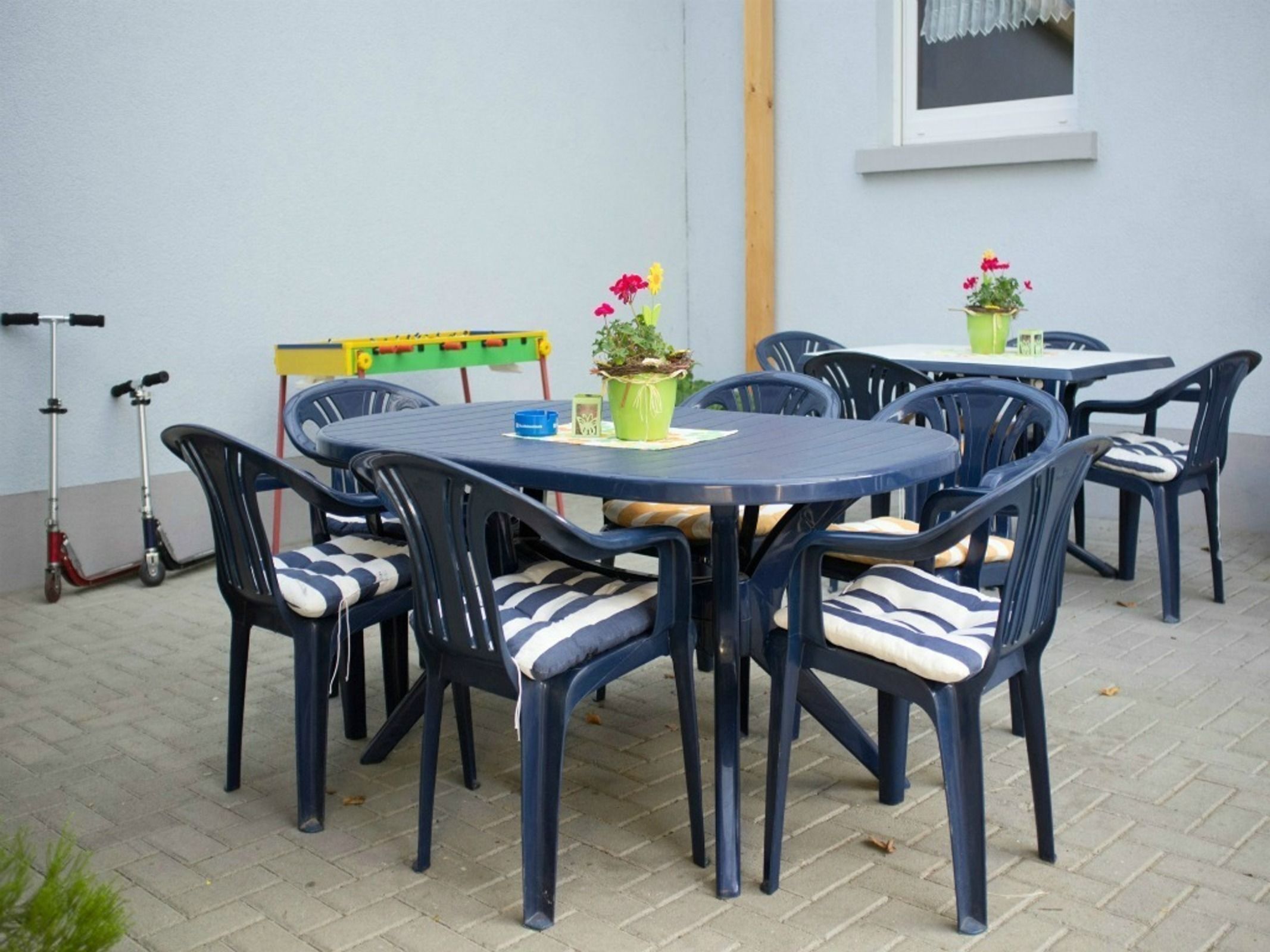 Un patio con mesas y sillas redondas, una pequeña estructura de juegos y un patinete.