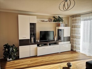Uma sala de estar moderna com televisão de tela plana, armários embutidos, uma mesa de centro de vidro e um vaso com planta.