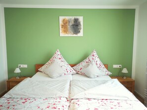 Uma cama com duas almofadas, uma parede verde e um quadro sobre a cama.