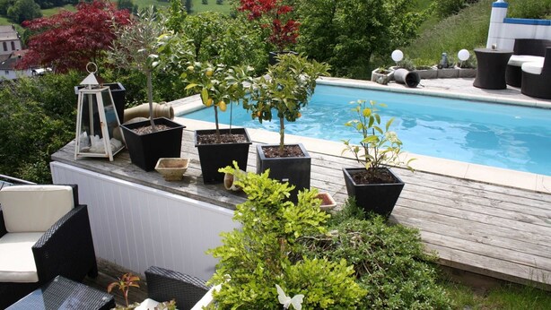 Ein Poolbereich mit Gartenmöbeln, Blumentöpfen und Blick auf die umliegende Landschaft.