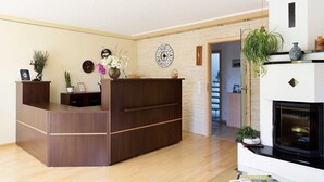 A reception area with a wooden desk, a clock, and a fireplace. - Standard family room - Pension Sieg (Rust)