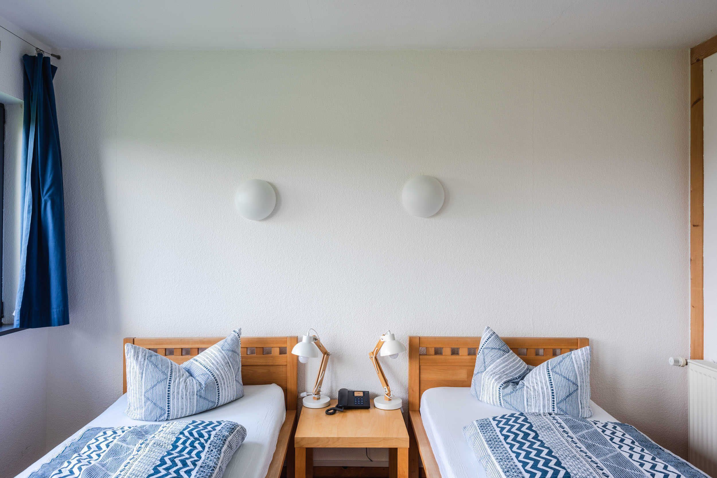 A twin room with two single beds, a wooden nightstand with lamps, a phone, and a small table.
