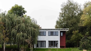 Een modern huis met twee verdiepingen, een plat dak, grote ramen en een gevel in wit en rood.