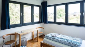 Een lichte, compacte kamer met een bed, een bureau en twee stoelen.