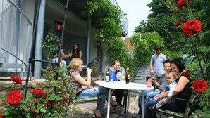 Un groupe de personnes est assis à une table en plein air, avec vue sur un jardin et un bâtiment en arrière-plan.