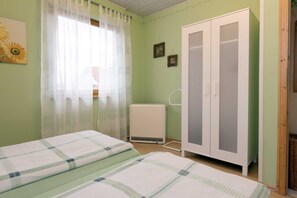 A bedroom with a bed, a wardrobe, a radiator, and a window with curtains. - Apartment 60 m² - Gästehaus Hauser (Rust)