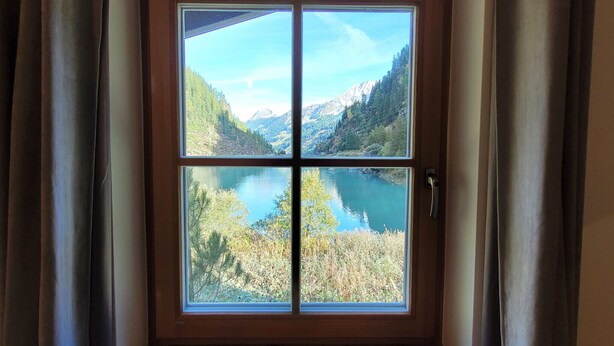 A four-pane window with a view of a mountainous landscape and a lake.