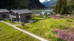A two-story building with a balcony, a small garden, and a view of a lake and mountains.