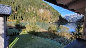 A view from a wooden cabin overlooking a calm lake surrounded by dense forest and mountains.