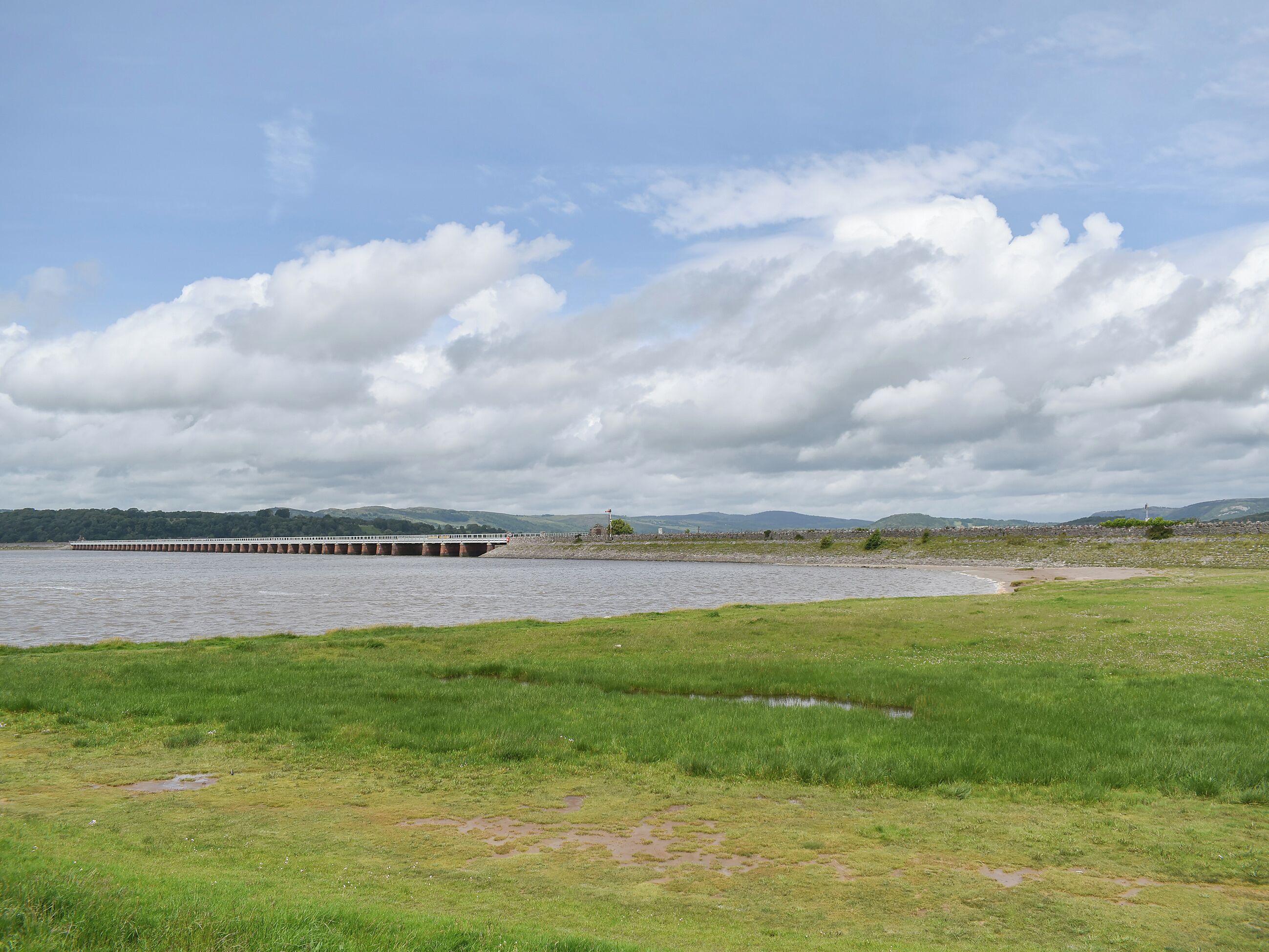 A bridge over a river with grassy banks and distant hills.