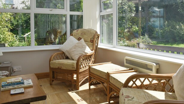 A conservatory with wicker furniture, a table with books, and a view of a garden. - 3 bedroom accommodation in Arnside, near Grange-over-Sands (Arnside, near Grange-over-Sands)