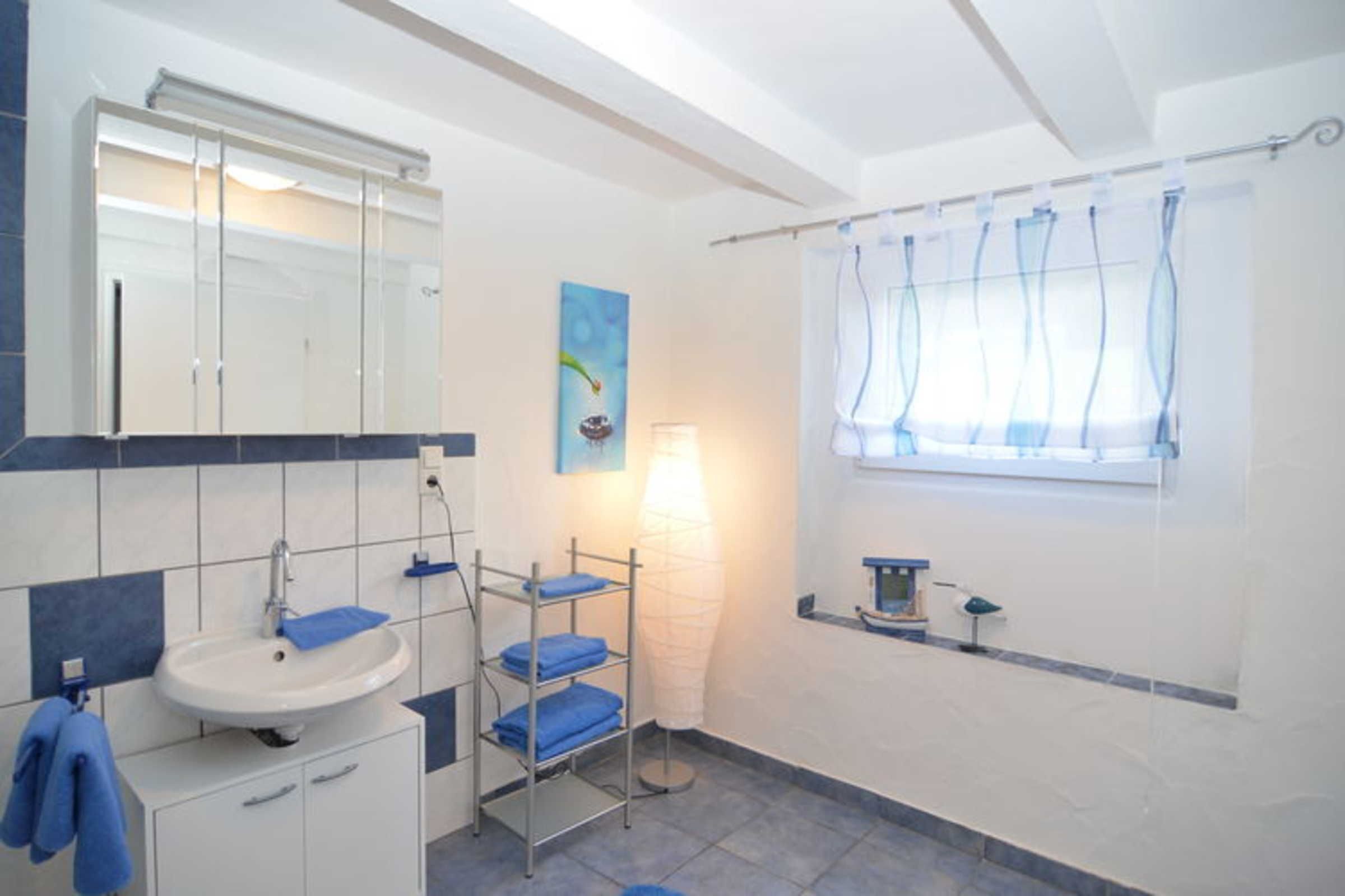 Un baño con lavamanos, espejo, toallero y ventana con cortinas.